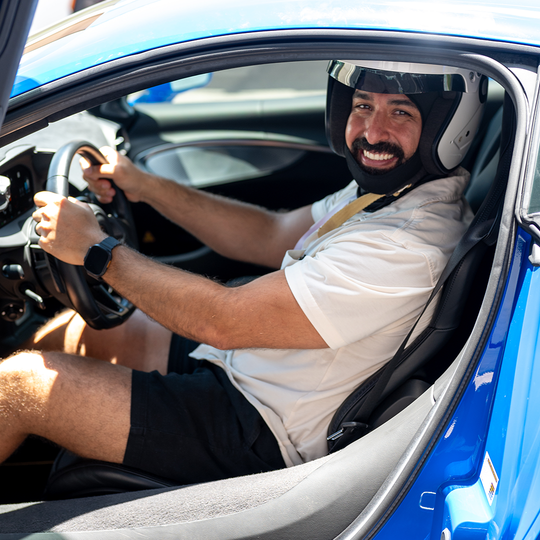 A helmeted driver smiling from the seat of a blue sports car.
