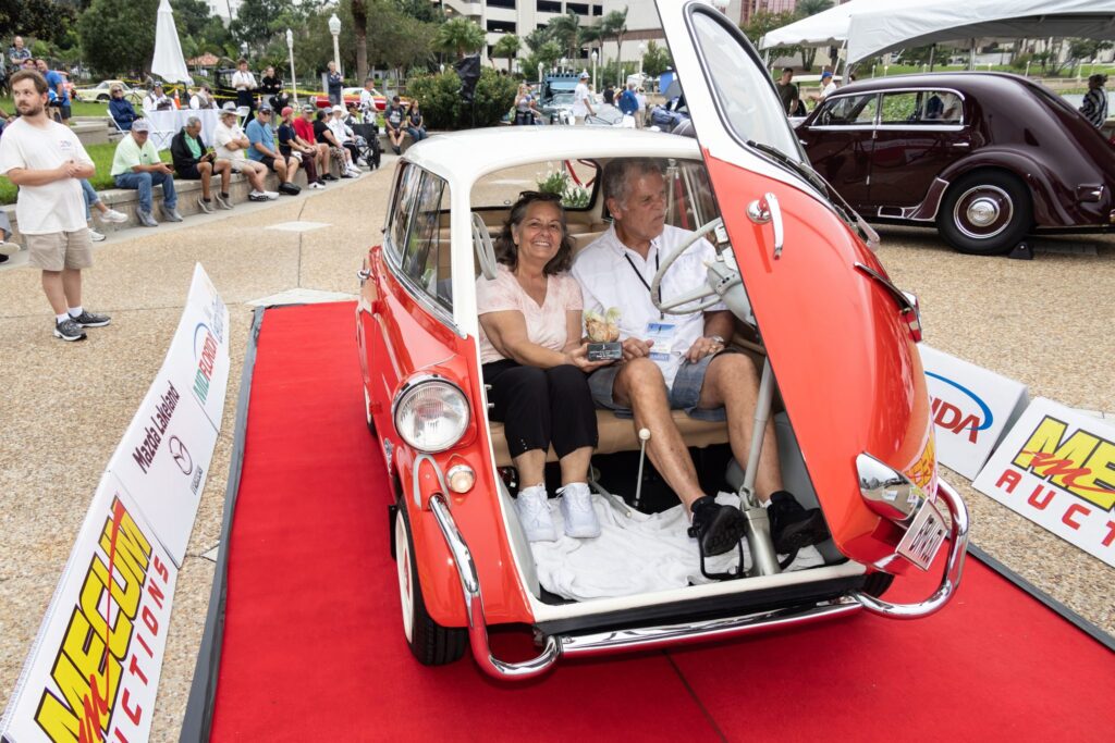 Two passengers smiling inside a microcar with its front door open